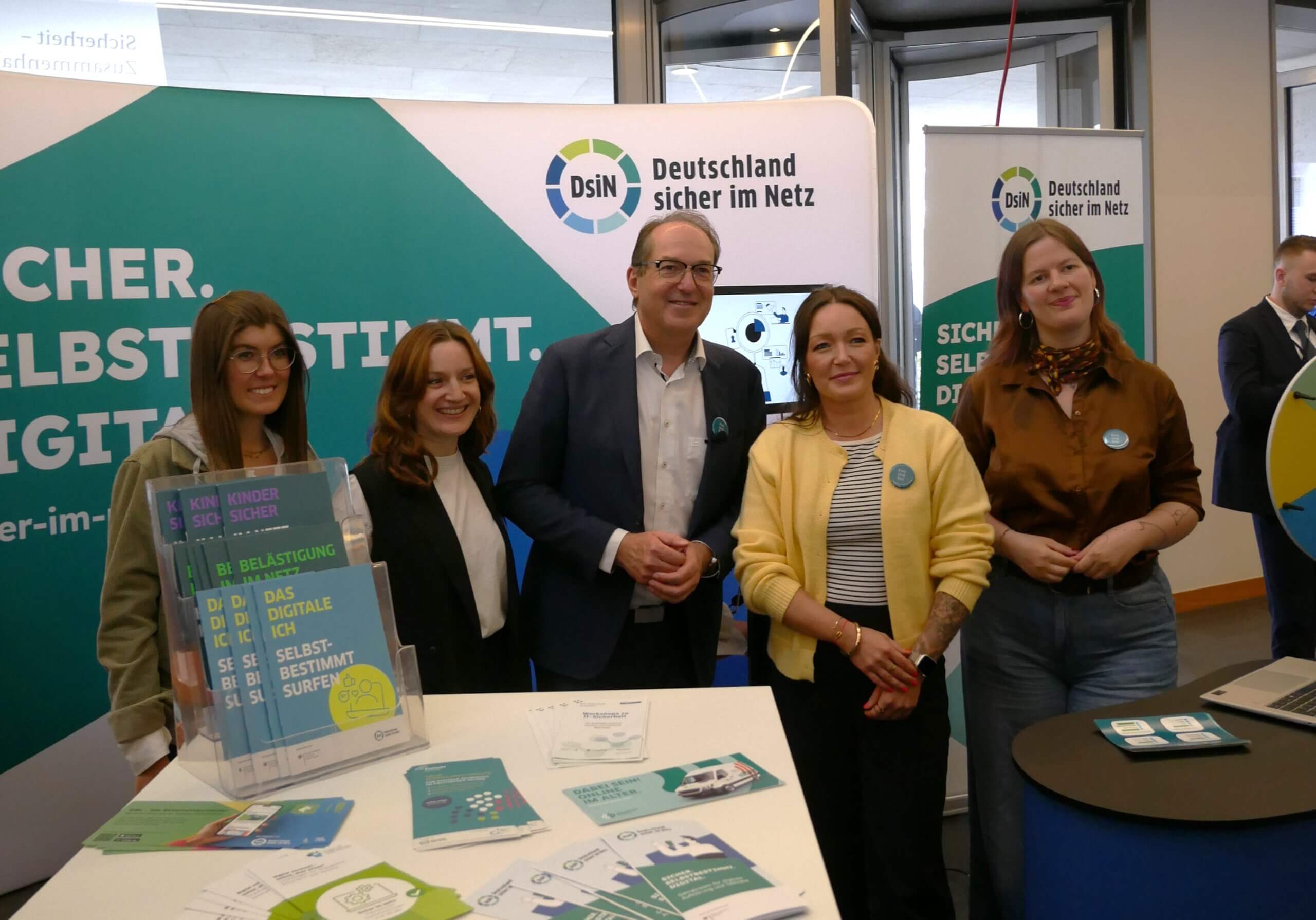 Foto vom Tag der offenen Tür der Bundesregierung aus dem BMI: Bundesinnenminister Alexander Dobrindt gemeinsam mit Mitarbeiterinnen von Deutschland sicher im Netz am Stand von DsiN