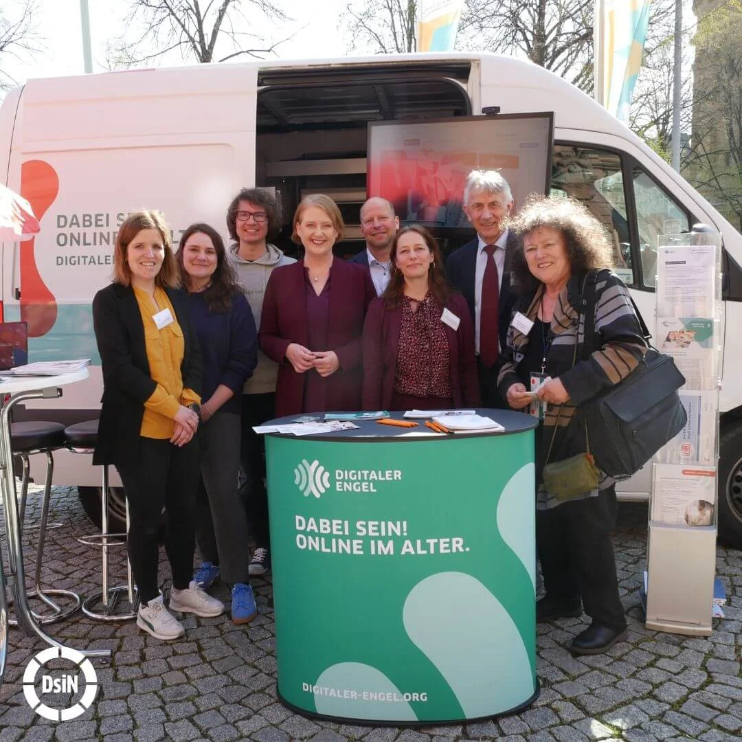Das Team des Digitalen Engels steht mit Bundesministerin Lisa Paus vor dem Infomobil des Digitalen Engels und lächelt in die Kamera.
